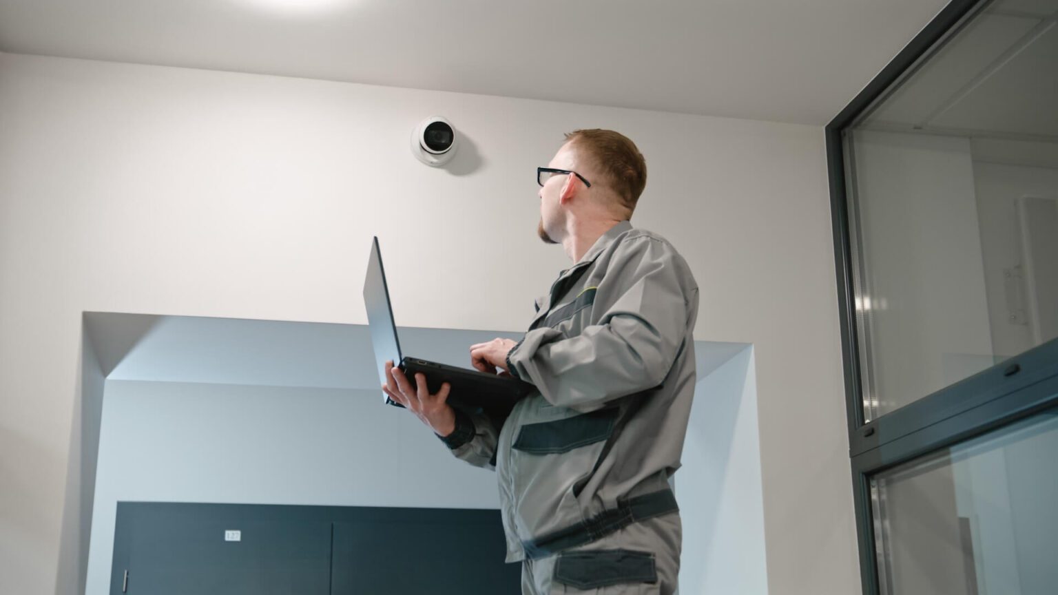 Un installateur en uniforme installe une caméra de sécurité dans un bureau à l'aide d'un ordinateur portable. Un homme portant des lunettes vérifie les caméras de télévision en circuit fermé dans un programme informatique. Système de surveillance. Concept de système de surveillance et de protection de la vie privée.